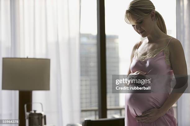 pregnant woman standing with hand on her belly - see through negligee stock pictures, royalty-free photos & images