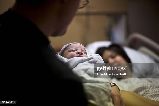 father carrying his newborn baby girl with his wife lying on a bed - young couple with baby stock pictures, royalty-free photos & images