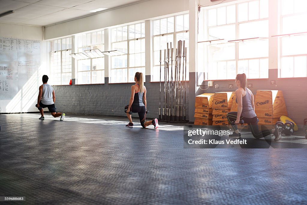 3 crossfitters doing lunges with small weights