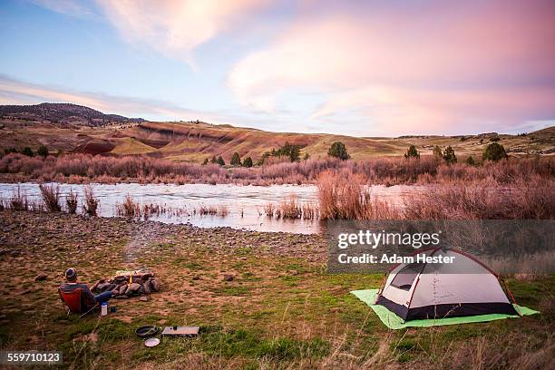 a young man camping with a tent next to a fire - 旁邊 個照片及圖片檔