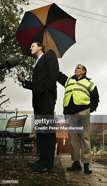 Local man holds an umbrella as Conservative Party Leadership challenger David Cameron gives a media interview whilst campaigning in Balsall Heath on...