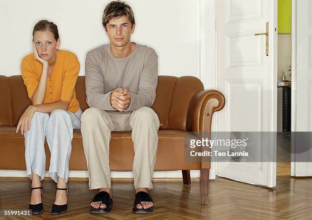man and woman sitting side by side on sofa - couple sitting stock pictures, royalty-free photos & images