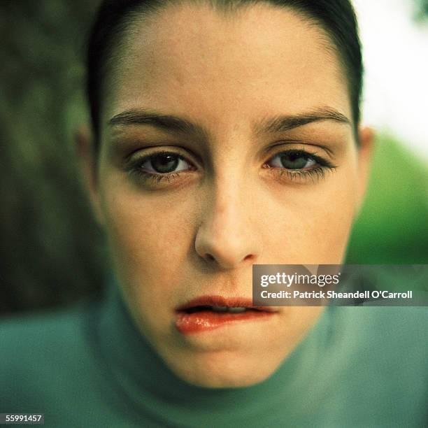 young woman biting lower lip, looking at camera, close up, portrait. - neid stock-fotos und bilder