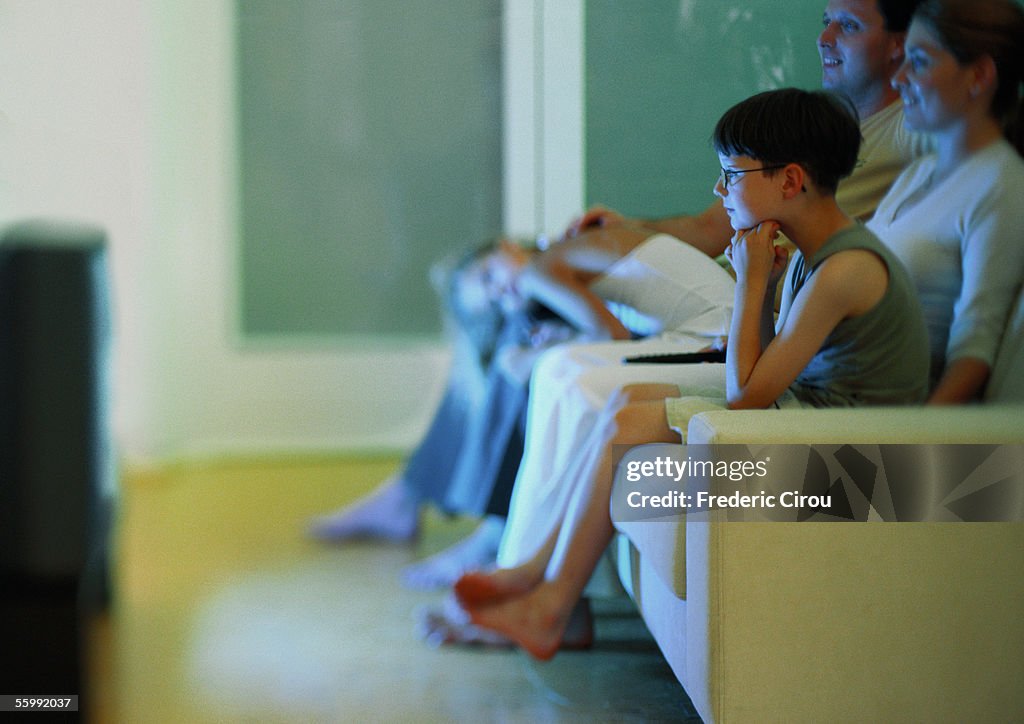 Family watching television on sofa, side view