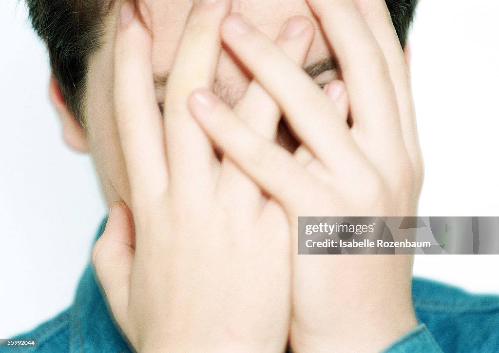 Teenage boy with hands covering face, close-up