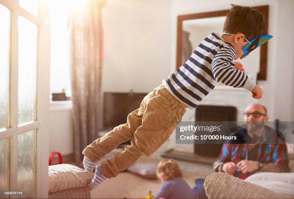 A young boy jumping from one sofa to another