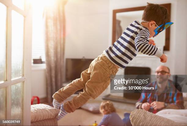 a young boy jumping from one sofa to another - misbehaving children stock pictures, royalty-free photos & images
