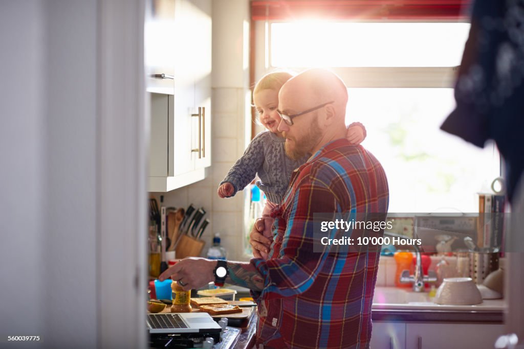 Man holding daughter whilst using laptop