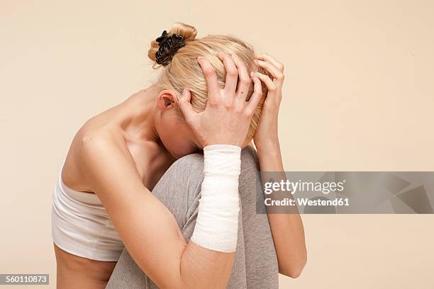 despaired young woman sitting with head in hands and bandage around arm - cutting yourself stock-fotos und bilder