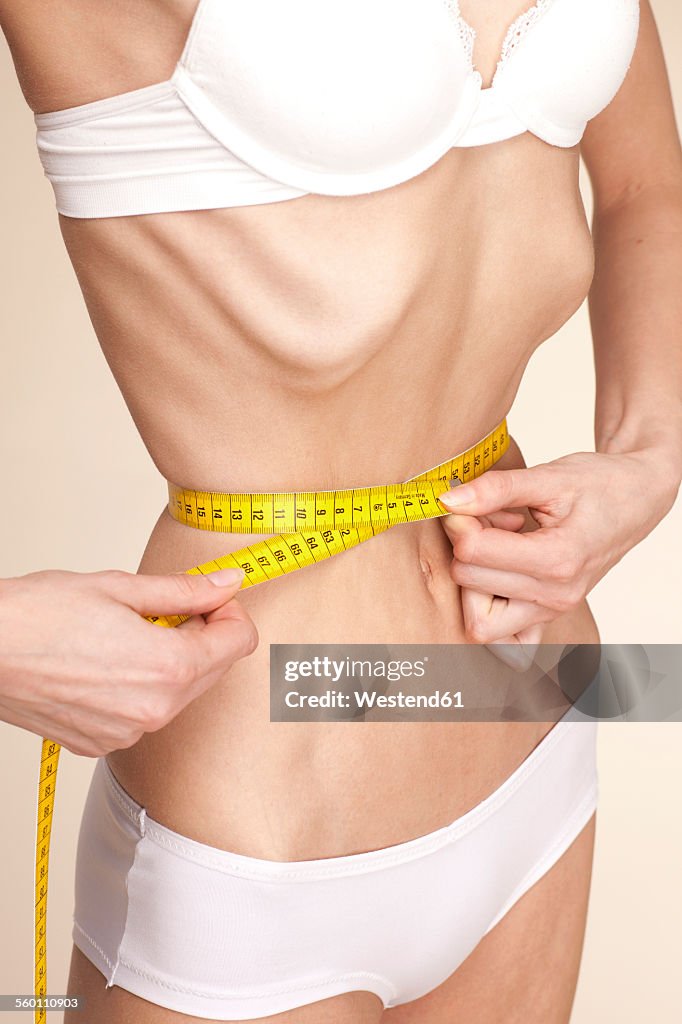 Anorexic young woman measuring her waist