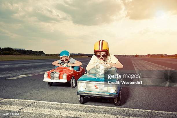 two boys in pedal cars crossing finishing line on race track - sports helmet foto e immagini stock