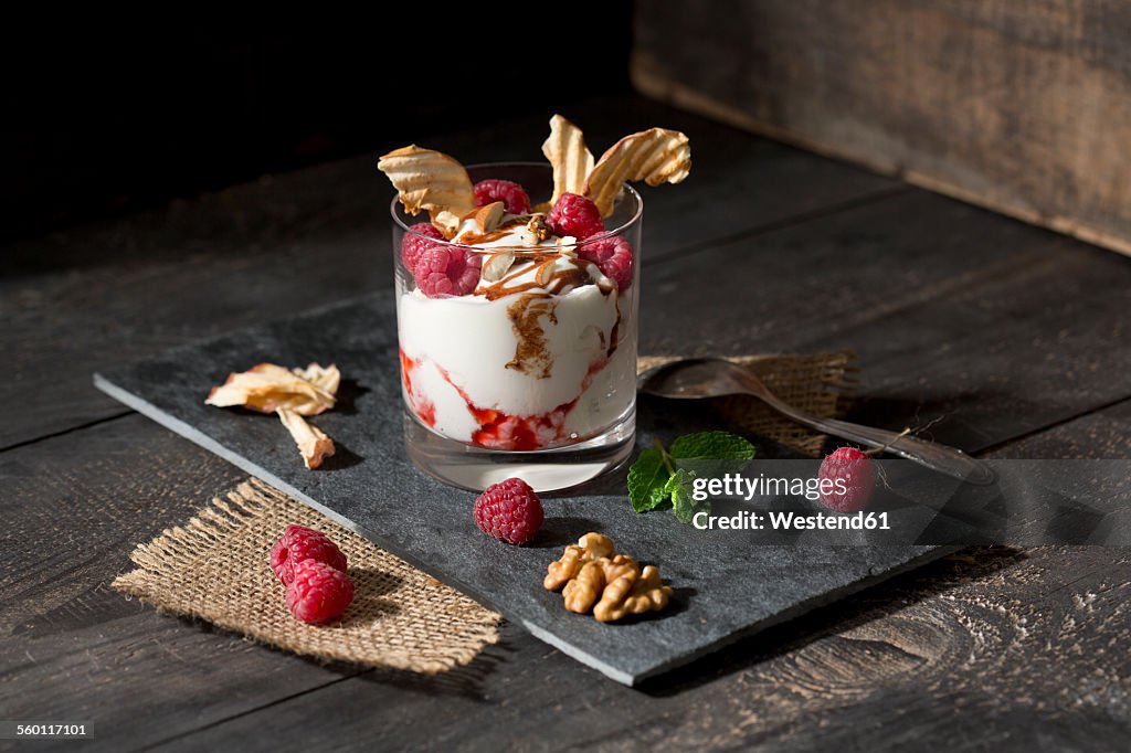 Dessert in glass with raspberries, curd, yoghurt, dried apple, almond slivers and chocolate sauce