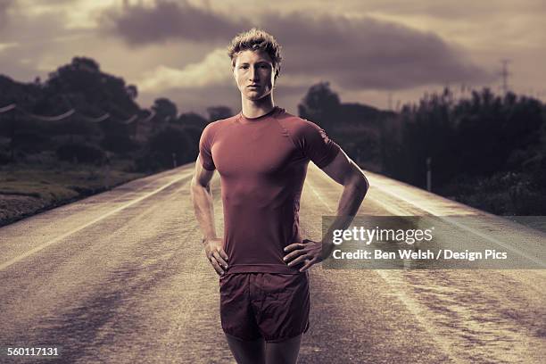 a young man poses in running shorts and t-shirt on a road - running shorts foto e immagini stock