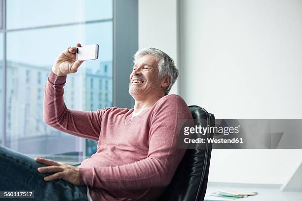 man sitting in a leather chair taking a selfie with his smartphone - solo un uomo foto e immagini stock