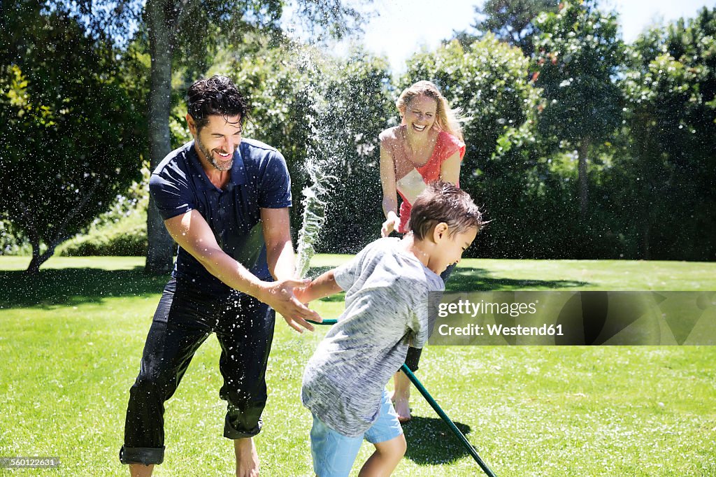 Happy family splashing water with garden hose