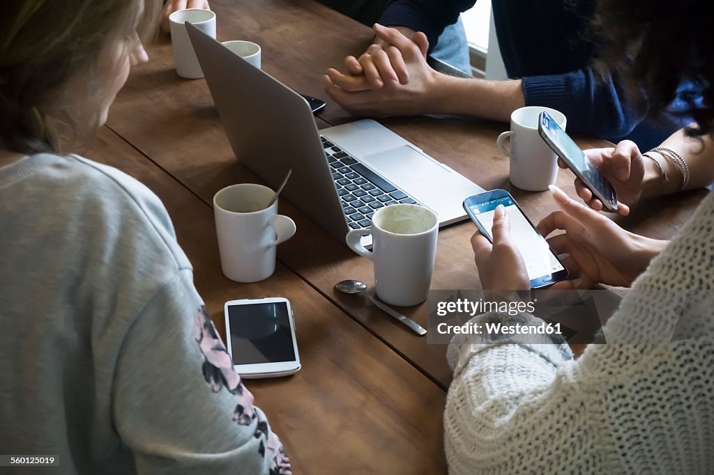 Group of friends with laptop using smartphones in a cafeteria