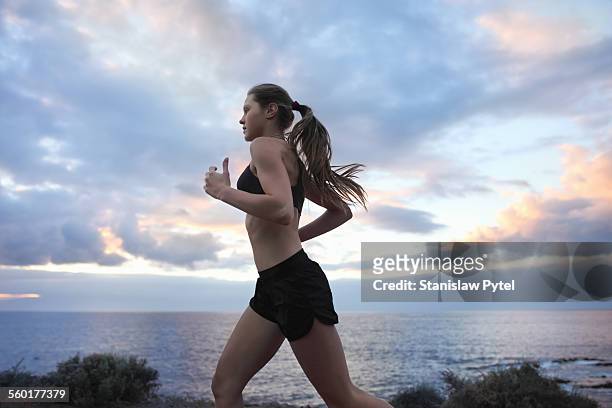 young woman running near ocean with cloudy sky - corriendo fotografías e imágenes de stock