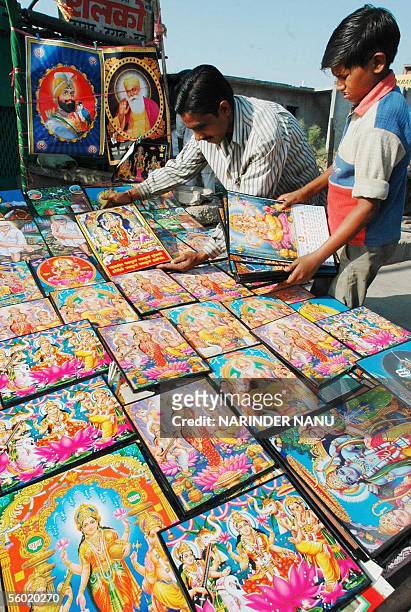 Indian vendors Nikku and Raju adjust pictures of Hindu Gods Laxmi and Ganesh at their road side stall, 27 October 2005 in Amritsar, in India's...