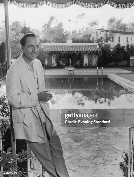 Suave American actor William Powell relaxes fully-clothed by a swimming pool, 1939.