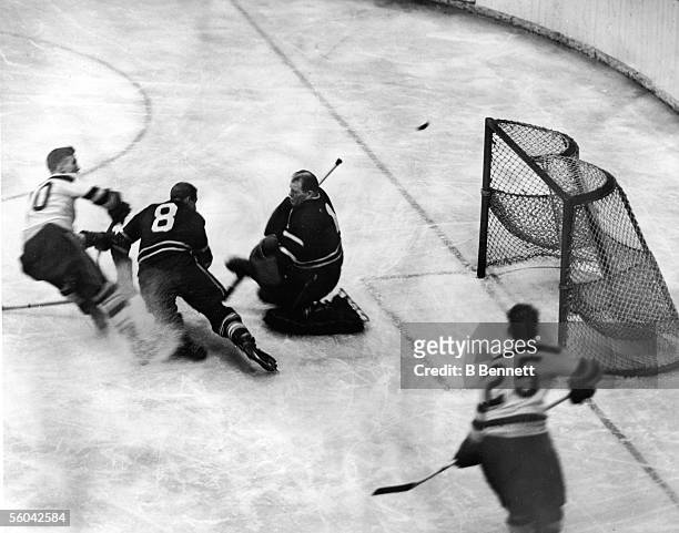 Canadian professional hockey player Walter 'Turk' Broda , goalie for the Toronto Maple Leafs, kneels in front of the goal post and attempts to block...