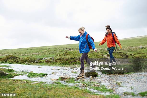two hikers crossing stream in countryside - raincoat stock-fotos und bilder