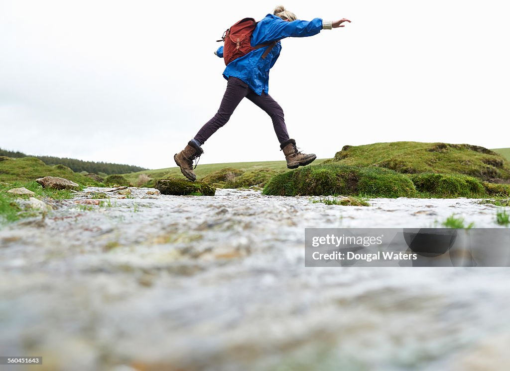 Hiker stepping across stream in countryside