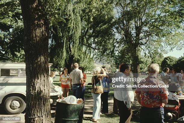 People picnicking in a park, a camper pickup truck in the background and a full garbage can in the foreground, on a sunny day, 1966.