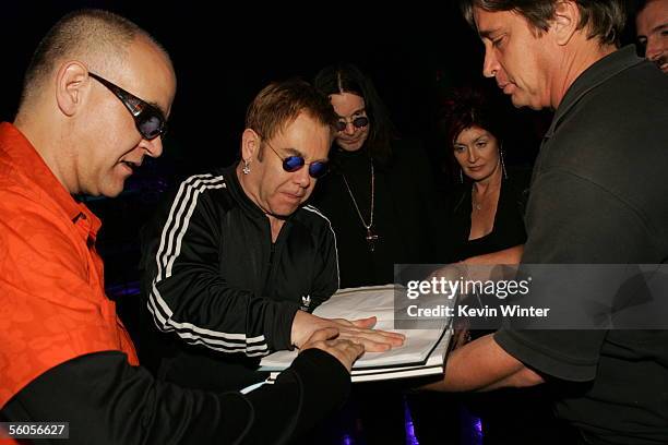 Sir Elton John makes his handprint in the official book under the watch of Ozzie and Sharon Osbourne as he records his contribution to the new...