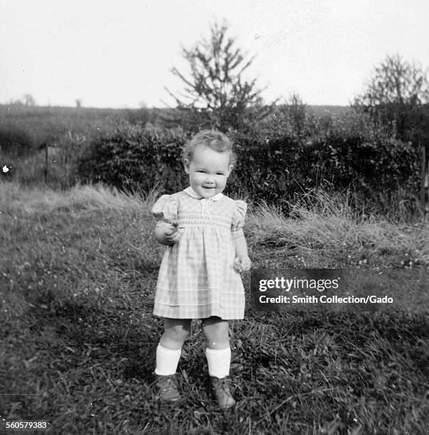 Smiling young girl wearing a checkered dress, standing in a garden, Germany, January 6, 1955.