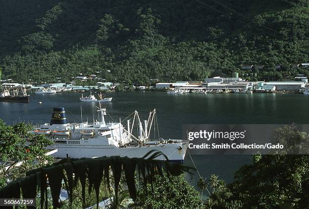 The cruise ship SS Mariposa, of the Pacific Far East Line, with iconic golden bear symbol, docked in a harbor with other boats and buildings, the...