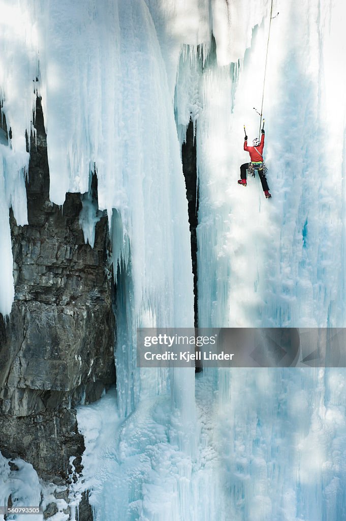 Male ice climber scales big ice-covered rock wall