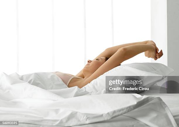 young woman in bed, stretching arms over head - woman pillow over head stock-fotos und bilder