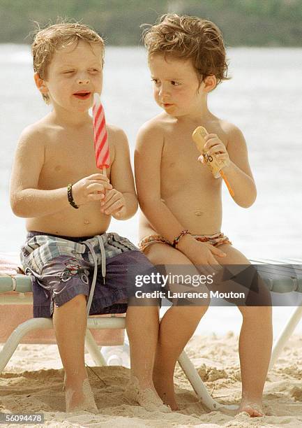 two children eating popsicles on beach. - neid stock-fotos und bilder