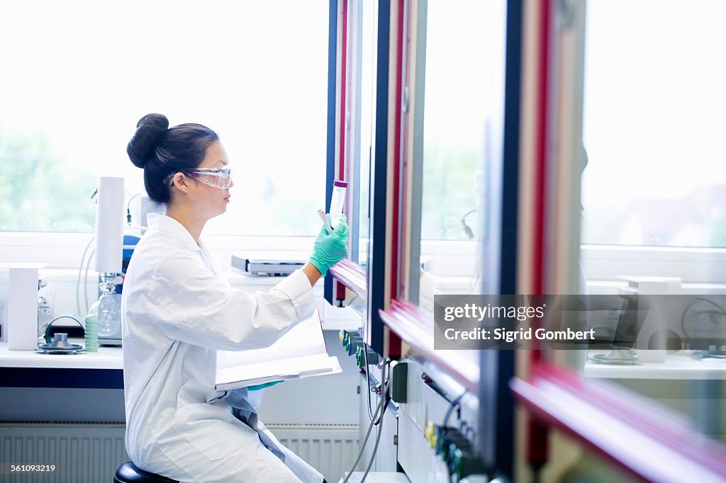 Young female scientist with notebook looking at sample in lab