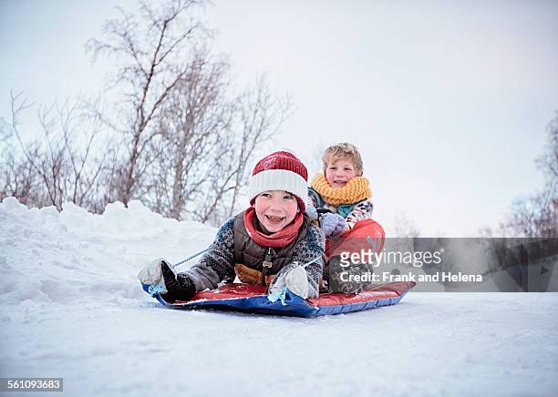 low angle view of two brothers on toboggan on snow covered hill, hemavan,sweden - hemavan stock pictures, royalty-free photos & images