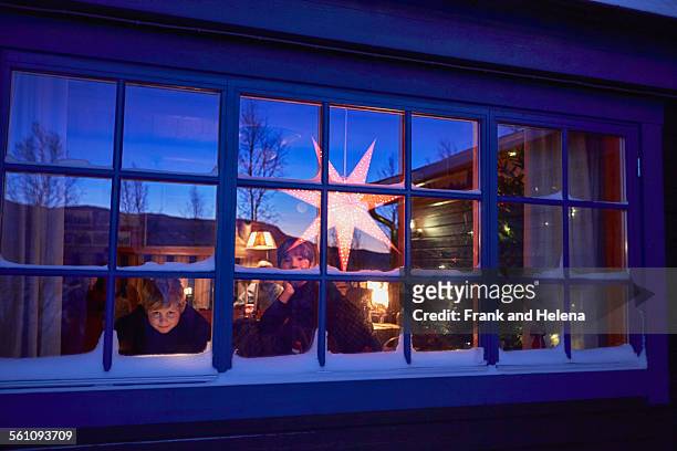 two brothers looking out of cabin christmas window at night - christmas scandinavia stock pictures, royalty-free photos & images
