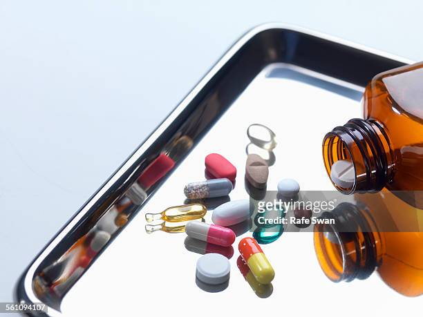 close up of variety of medical drugs pouring from pill bottle on surgical tray - antibiotic pills stock pictures, royalty-free photos & images