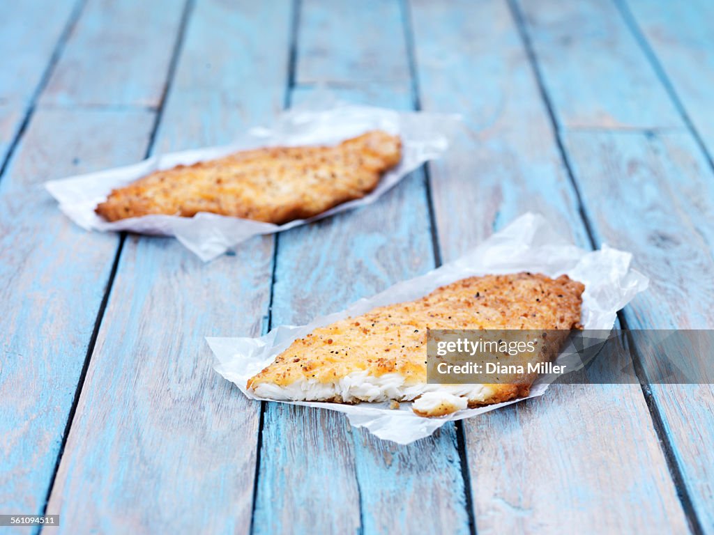 Two fried breaded flounder fish pieces on wooden table