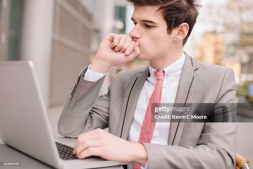 Worried young city businessman using laptop at sidewalk cafe