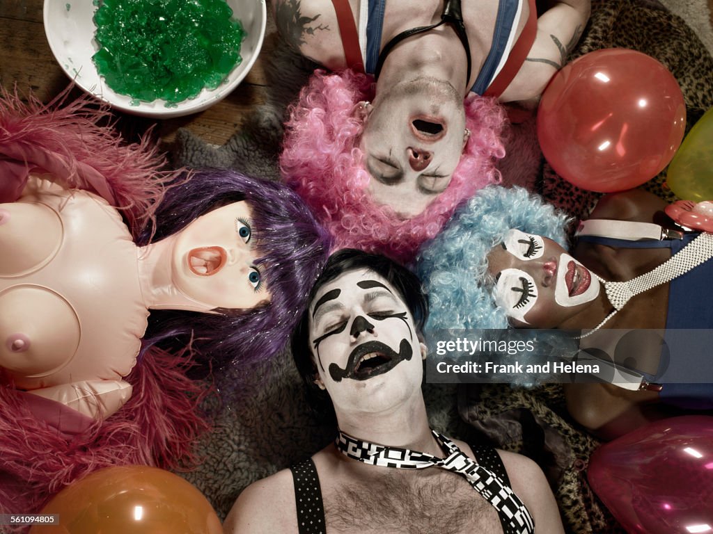 Overhead view of three adults wearing clown face paint and wigs with blow up doll