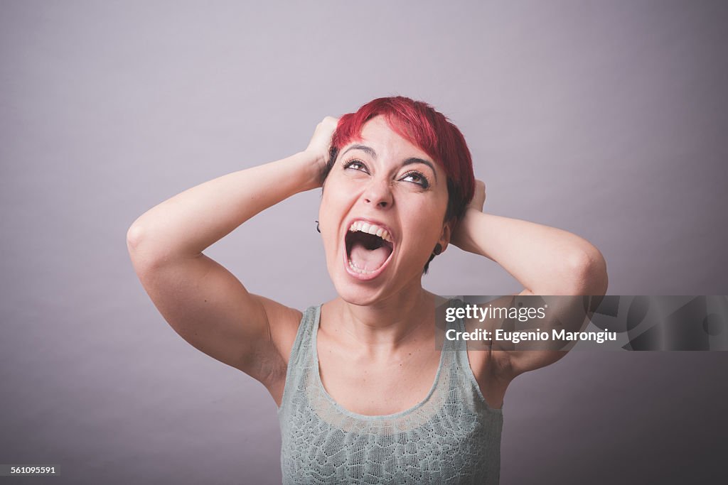 Studio portrait of young woman with hands in hair shouting