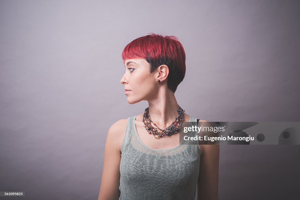 Studio portrait of young woman with short pink hair looking over her shoulder