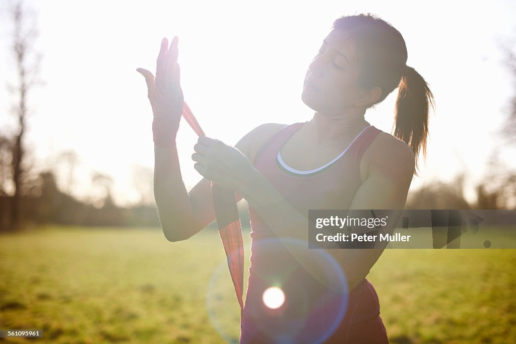 Mature female boxer bandaging hands in field