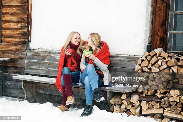 two young female friends drinking coffee outside wooden cabin - tirol deelstaat stockfoto's en -beelden