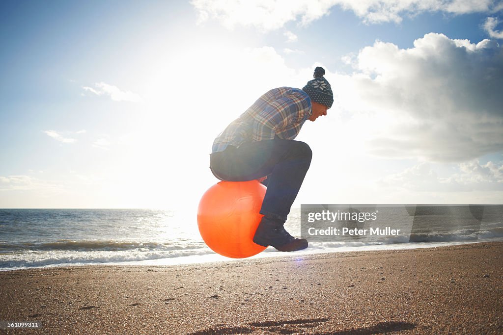 Mature man jumping mid air on inflatable hopper at beach