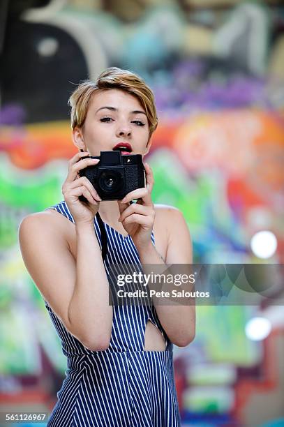 portrait of cool teenage girl holding up camera in front of graffiti wall - pete vandal stock-fotos und bilder