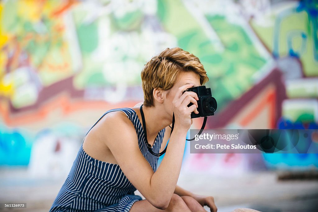 Stylish teenage girl photographing with camera in front of graffiti wall