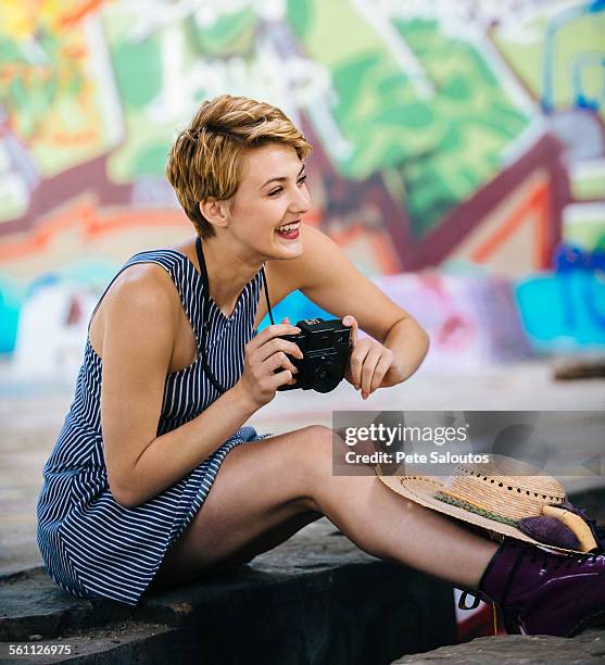 stylish teenage girl sitting on sidewalk with camera in front of graffiti wall - pete vandal foto e immagini stock