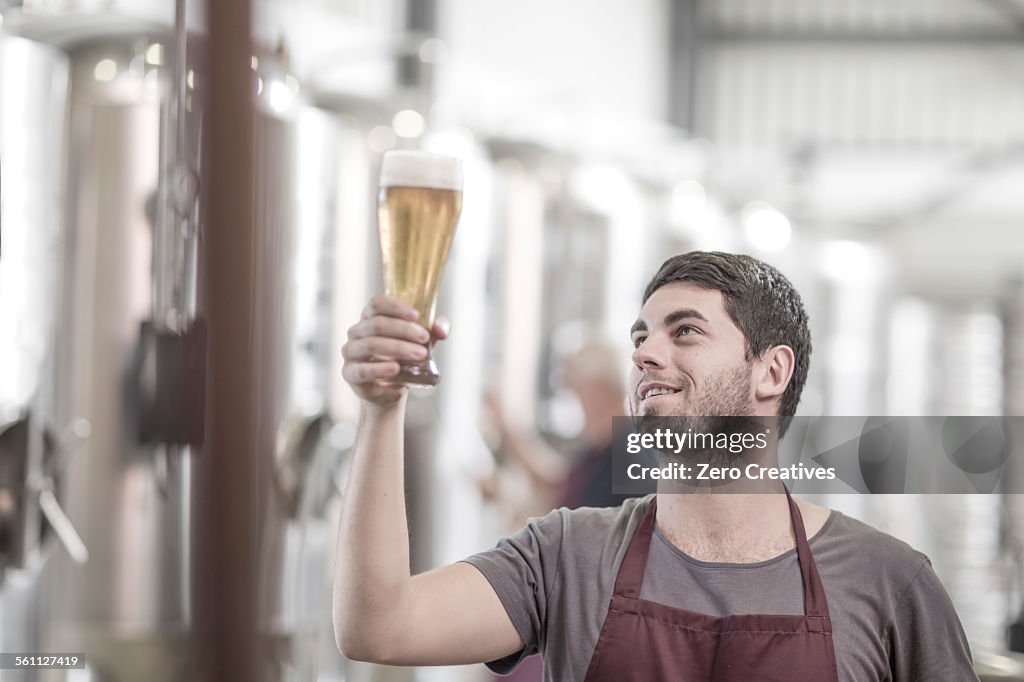 Brewer in brewery holding up a glass of beer