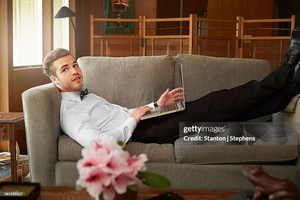 Portrait of man wearing smart clothes laying on sofa using laptop